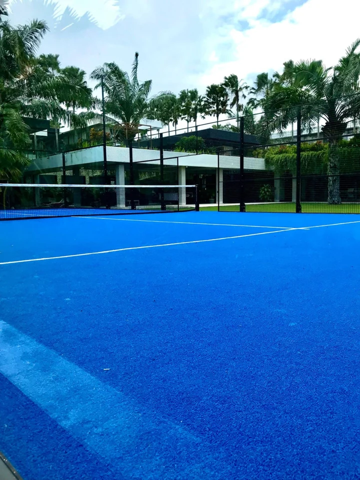 Blue padel court enclosed in glass with tropical trees beyond